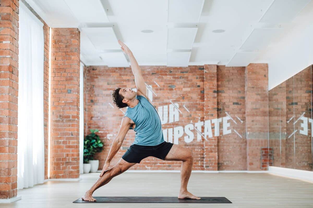 Man in Warrior 2 yoga pose looks strong in Upstate Studios heated mat room.