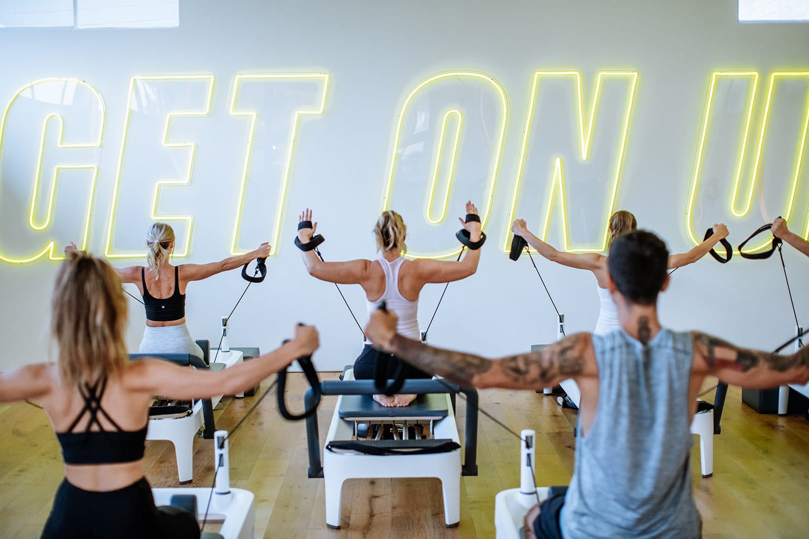 Reformer Pilates room is full of happy people exercising together in at Upstate Class. An aesthetic studio interior creates an uplifting space to workout.