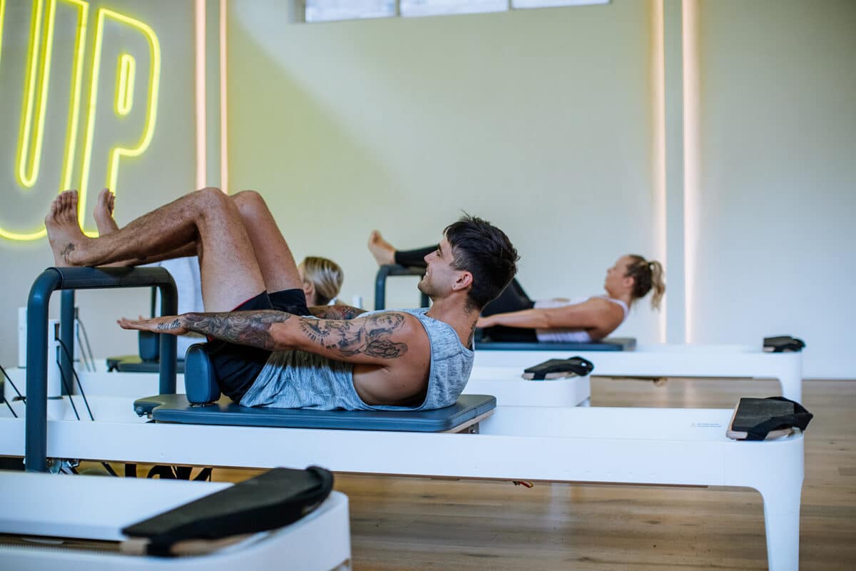 Strong man with tattoos works out on reformer, doing pilates at Upstate Studios.