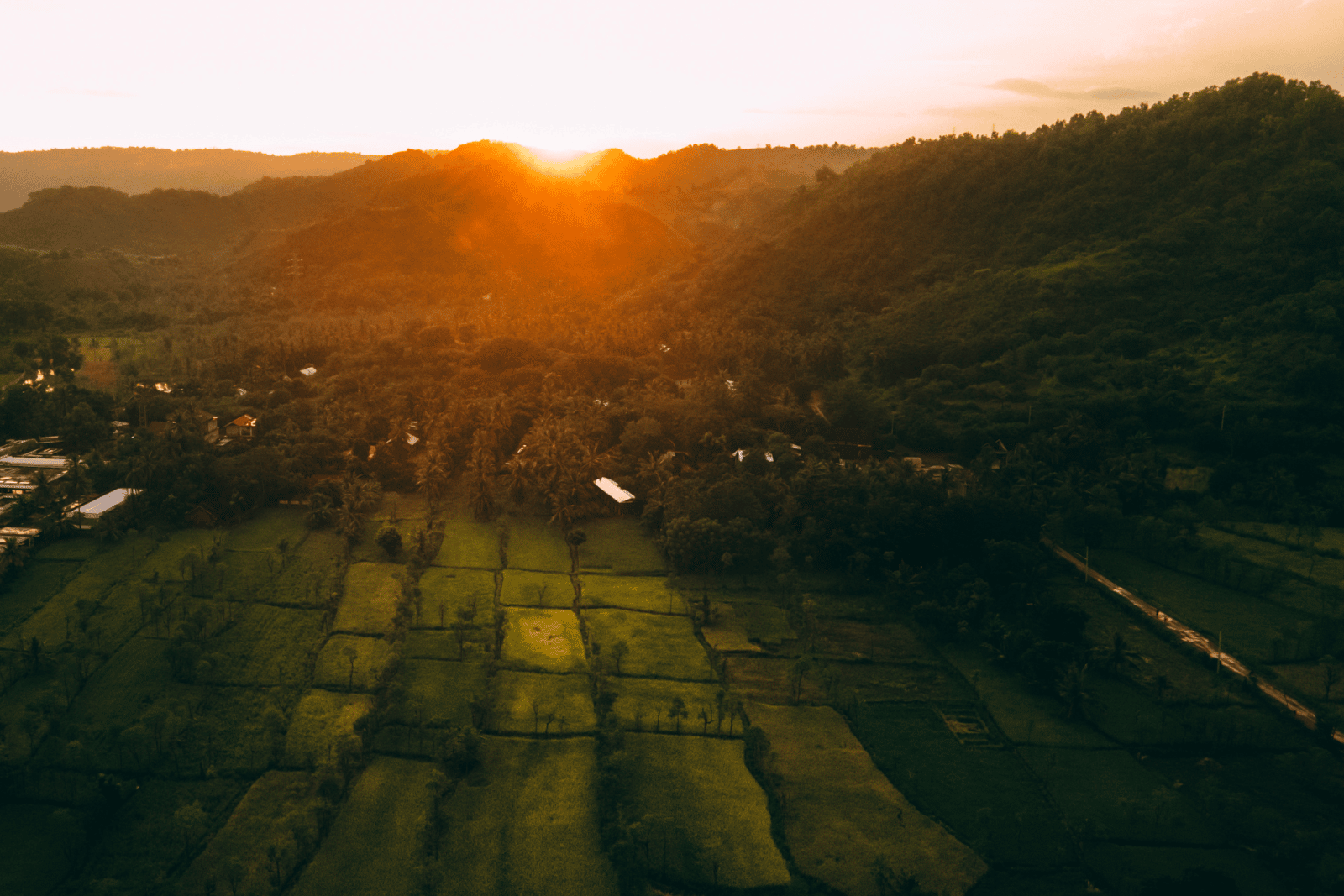 A sunset covers the green hills of Bali in a golden glow. From the arial view, we see Hotel Komune below, where Upstate Studios is hosting a stunning retreat.