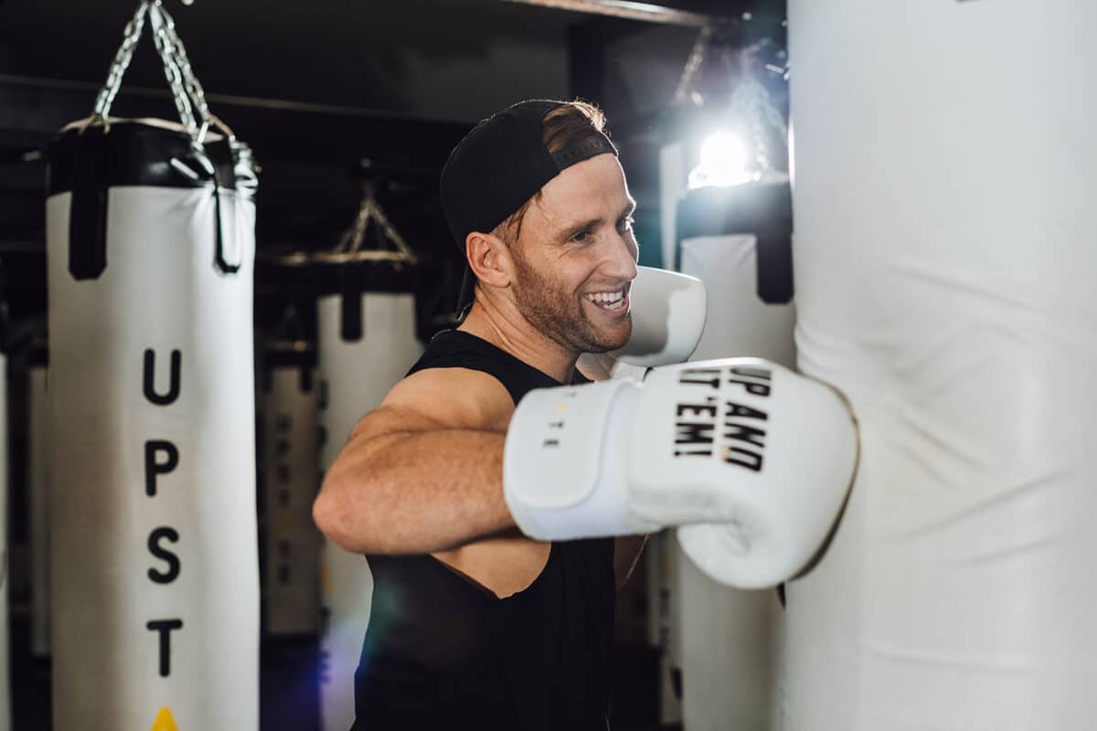 Upstate fitness instructor smiles as he punches a boxing bag in Upstate's dark box room.