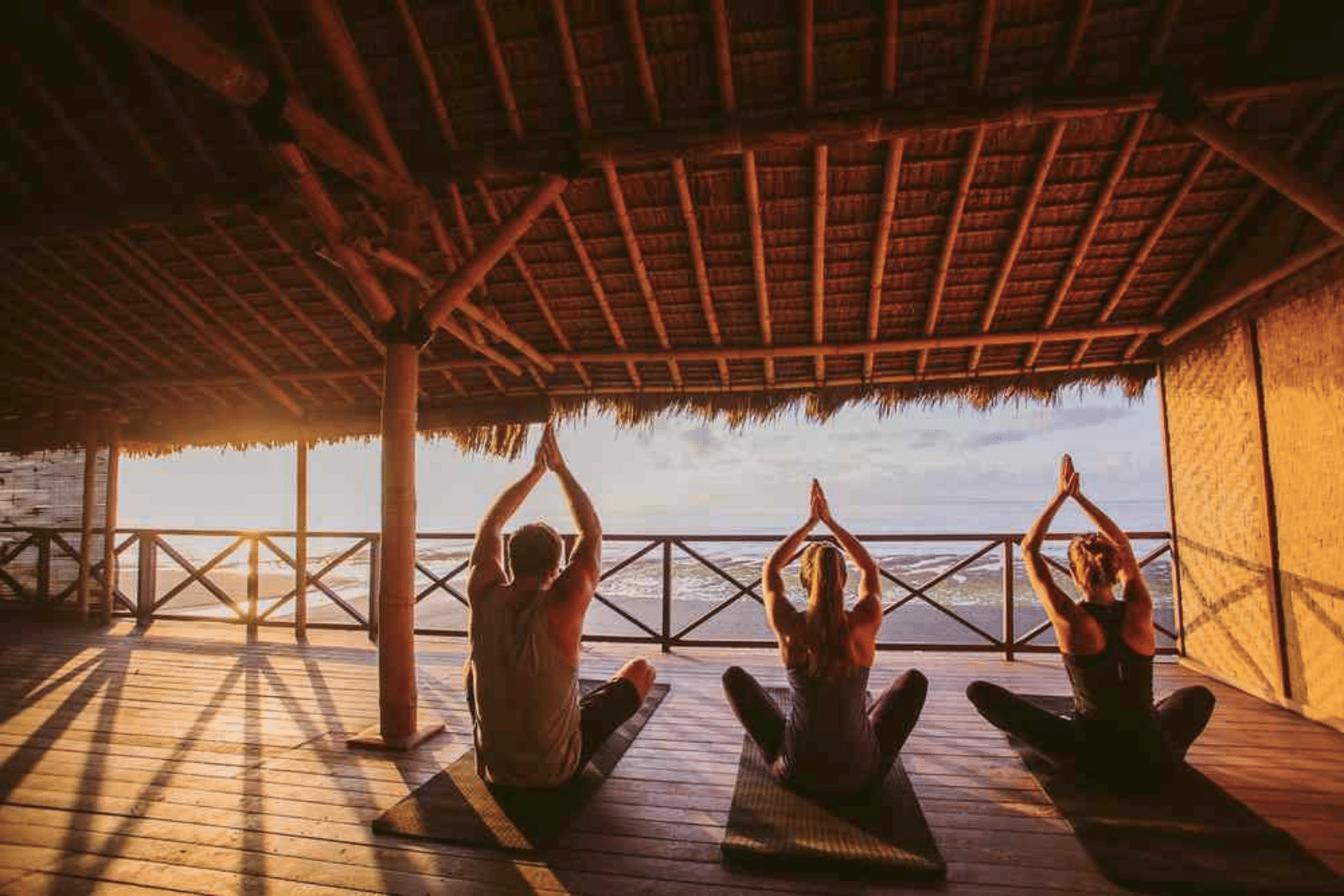 People on an Upstate Studios Retreat raise their hands in prayer towards a stunning sunrise in an open air shala at Hotel Komune Bali.