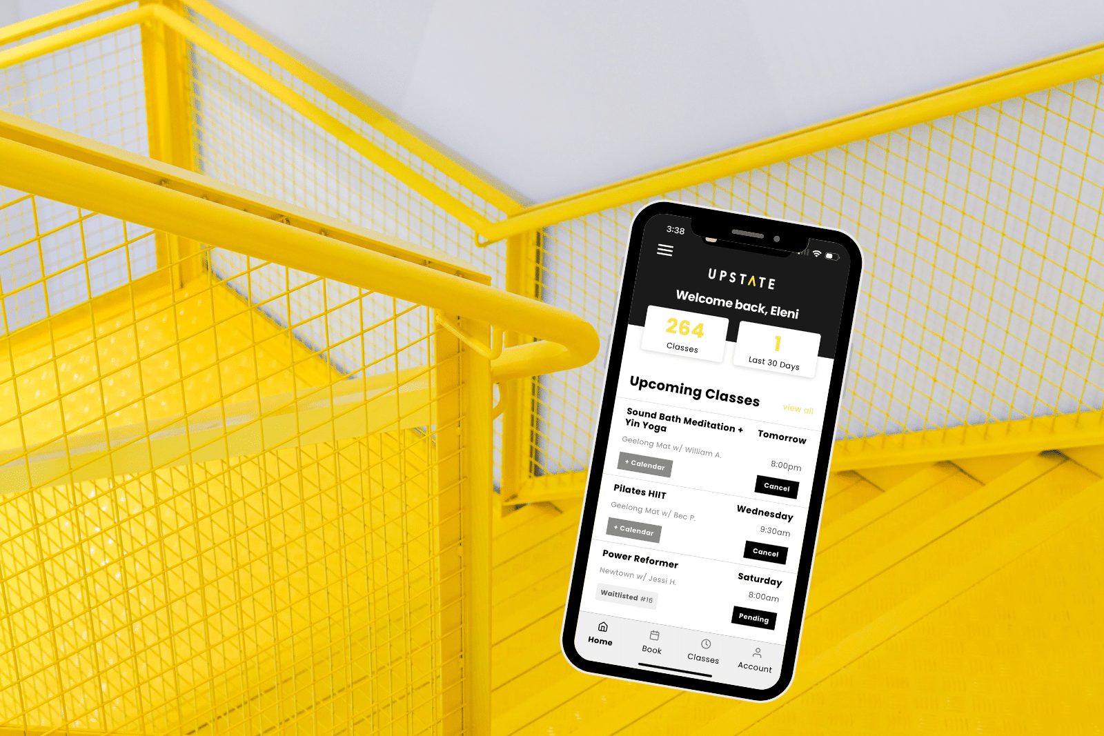 Phone displays Upstate Studio App used to book classes. Background is happy yellow staircase in interior of Upstate space.