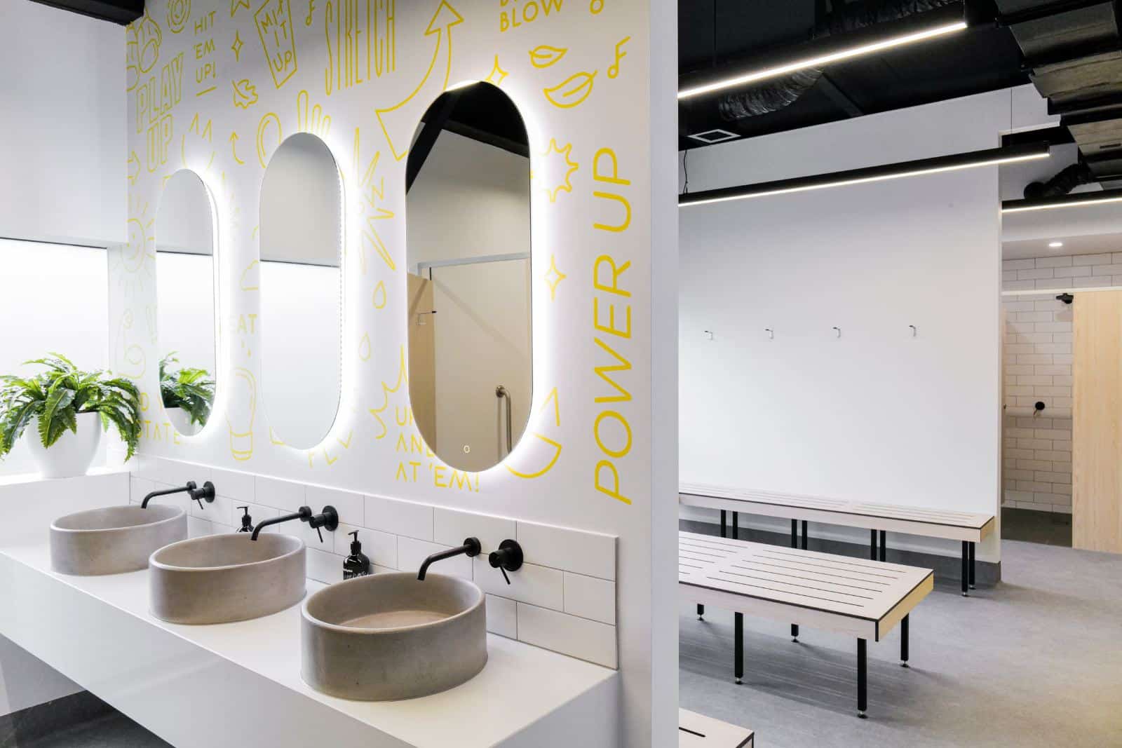 Fresh and clean changerooms at Upstate Studios. Walls are white and covered in yellow uplifting graphics. The mirrors have great lighting and high end hair tools and quality shower products are stocked in the space.
