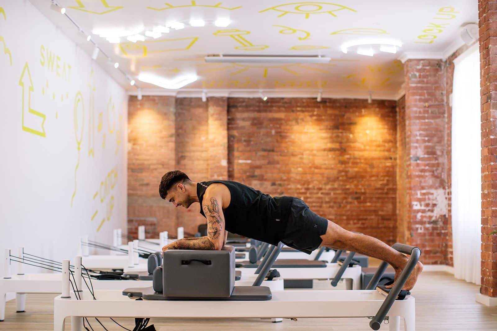 Man gets strong as he does a plank on a reformer bed at Upstate Balaclava. He works out happily in a cool motivating fitness studio space.